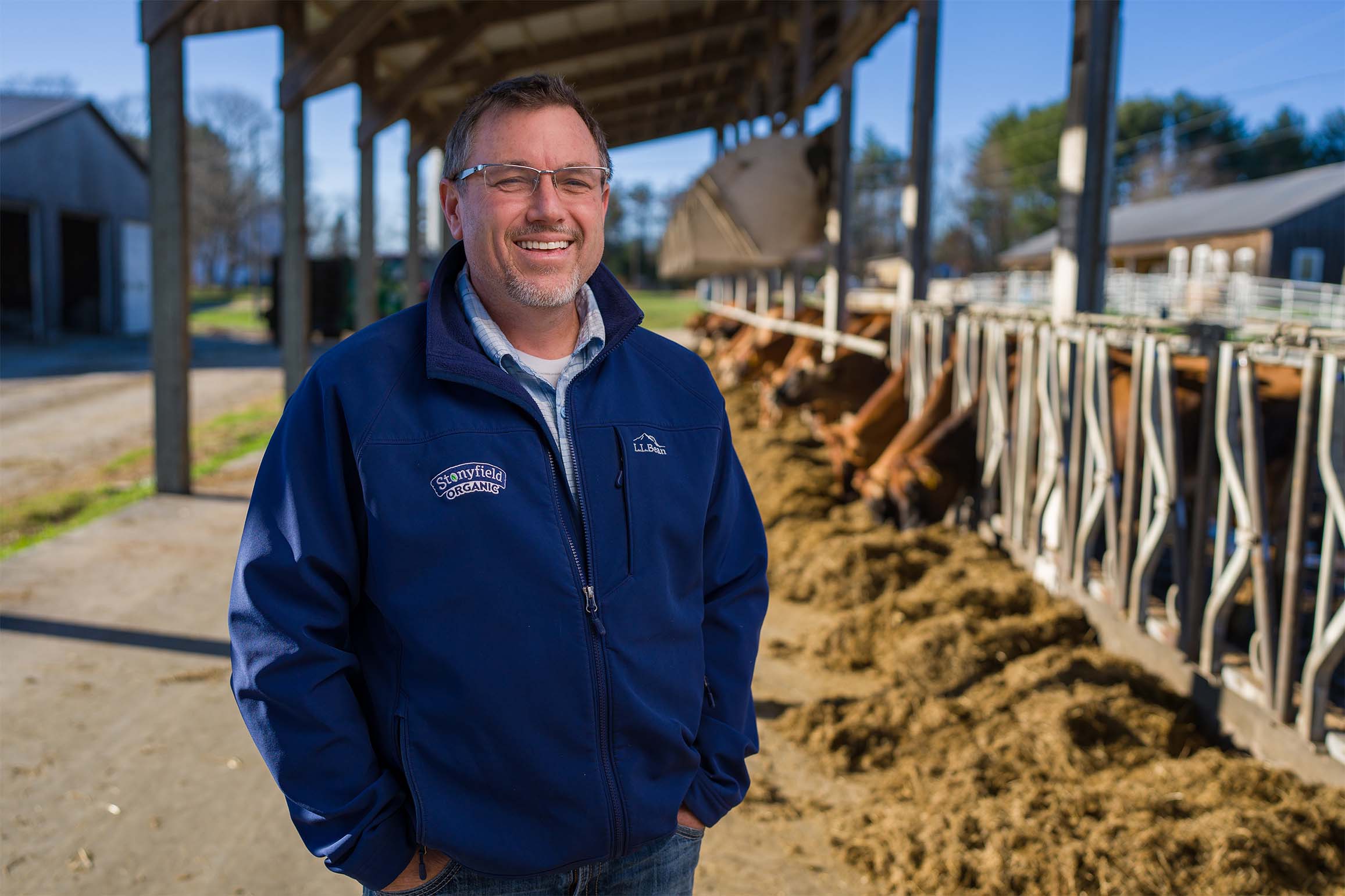 COLSA alum Jason Johnson '96 smiles at the camera while standing in front of the feed stalls at the UNH Organic Dairy Research Farm in Lee, N.H.