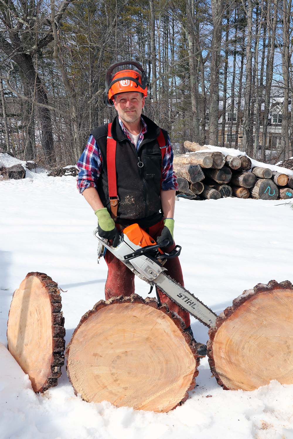 UNH woodlands manager Steve Eisenhaure stands holding his chainsaw with tree cookies in front of him while at the UNH Sawmill.