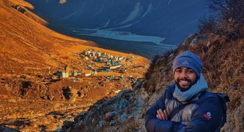 A photo of a man, Sandesh Lamichhane, standing in the mountains in front of a mountain village.