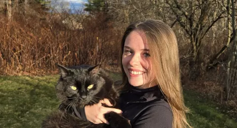 UNH undergraduate Kaley Dupont poses outside with a black cat