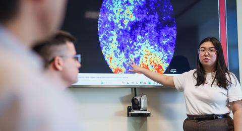 Graduate student pointing to microscopic image of a mouse brain that's being projected onto a large screen while two people look on