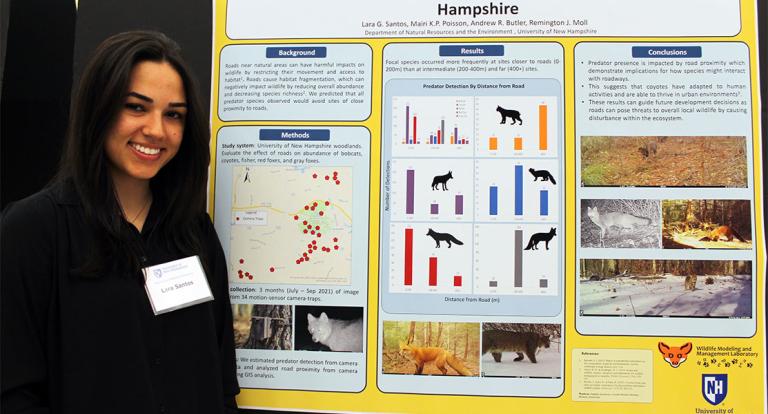 A photo of COLSA student Lara Santos standing in front of her poster presentation at the 2022 Undergraduate Research Conference