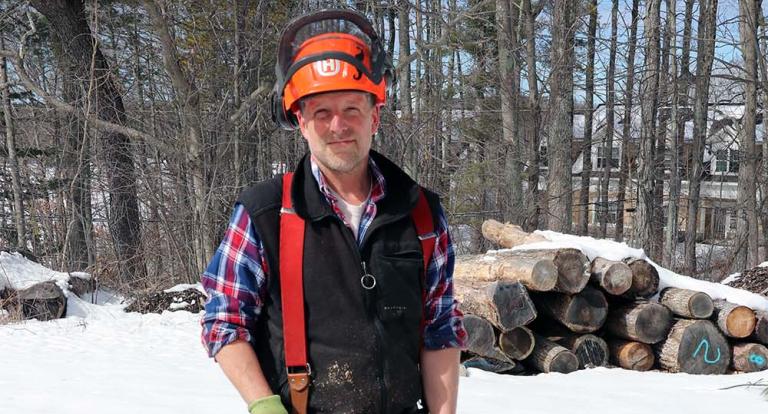 UNH woodlands manager Steve Eisenhaure stands holding his chainsaw with tree cookies in front of him while at the UNH Sawmill.