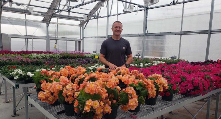 Luke Hydock, UNH greenhouse manager, standing amid rows of flowers at the Macfarlane Research Greenhouses.