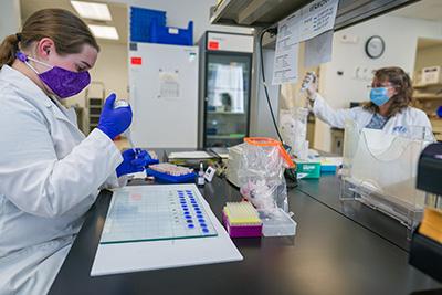 Student pipetting samples with Janet Poff working in the background