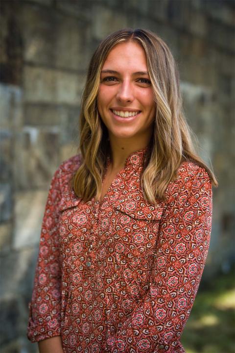 Master of Science in Nutrition student Abigail Moser. Abigail has tanned white skin, wears a red floral print top, has long brown hair. She is smiling.