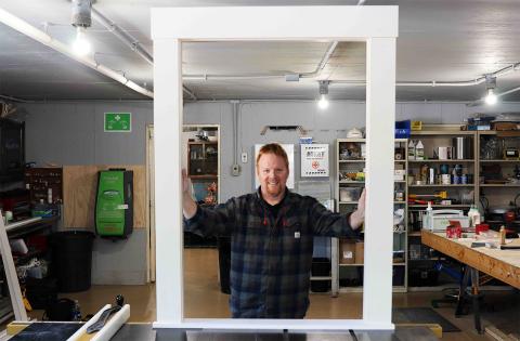 A photo of carpenter Curtis Johnson holding up a window frame that he fabricated at his shop on the UNH Durham campus.