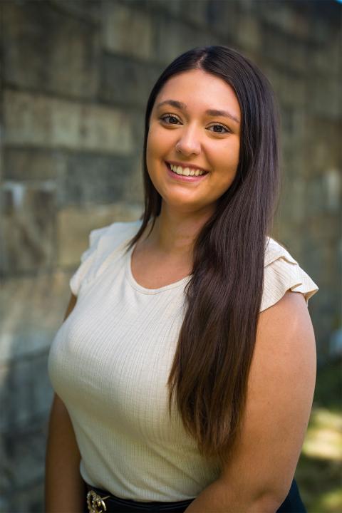 Master of Science in Nutrition student Emily Butkus. Emily has light brown skin. Her hair is a deep brown color and falls down to her elbows. She wears a cream-colored top.
