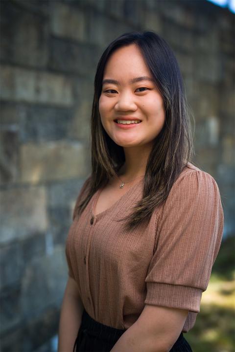 Master of Science in Nutrition student Lillian Huynh. Lillian has light brown skin. Her hair is mostly black. She wears a almond-brown top and black pants.