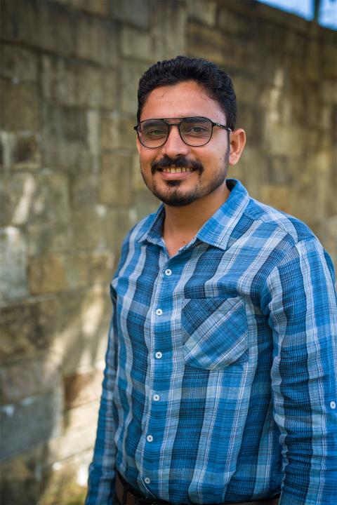 Master of Science in Agricultural Sciences student Muhammad Adeel Arshad. Adeel has brown skin and black hair. He has glasses with dark-brown frames. He wears a plaid-patterned shirt of light and dark blue.