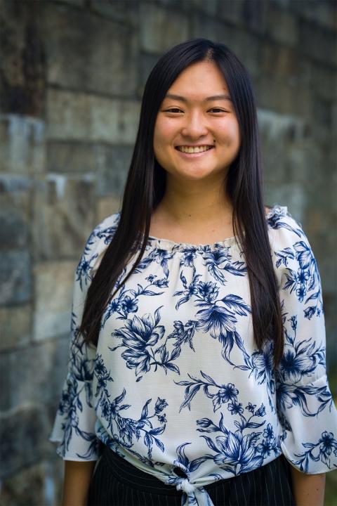 Master of Science in Nutrition student Tonya Xie. Tonya has tannish-brown skin. She has jet-black hair that falls to her elbows. She wears a blue-and-white floral print top and black pants.