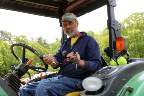 A photo of UNH farm manager Evan Ford holding up items while seated in a green tractor.