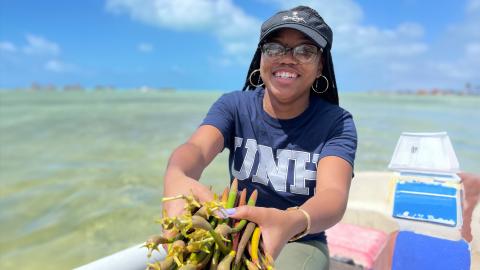 A photo of a black woman wearing glasses and holding some seaweed in her hands.