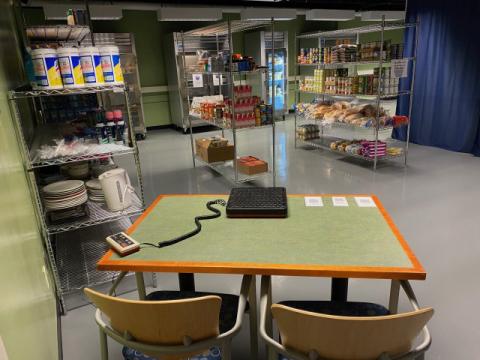 A photo of a table and, in the background, metal shelves of a food pantry.