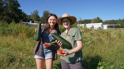 Two COLSA student farmers hold vegetables that they grew as part of UNH’s Farm to You program.