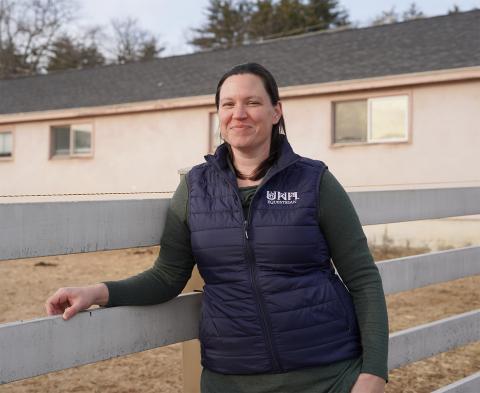 UNH Equine Center manager Erin Morgan-Paugh stands in front of a fence at a horse paddock at UNH.