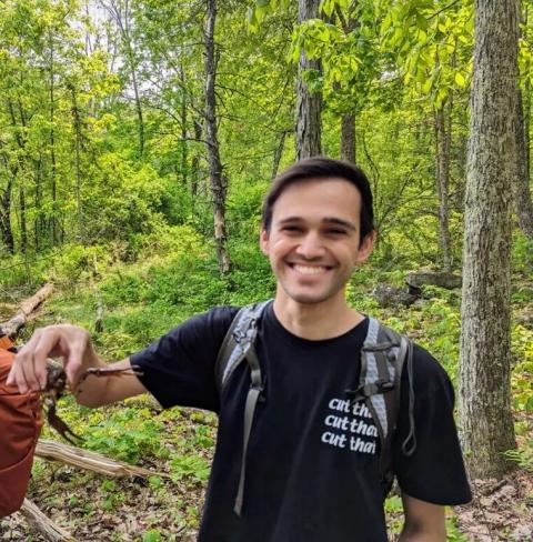 A photo of UNH alum Alex Zager in a forest holding up an animal.