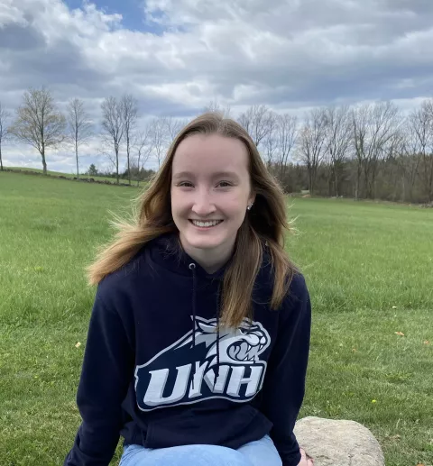 UNH student Olivia Audet in a field wearing a UNH sweatshirt
