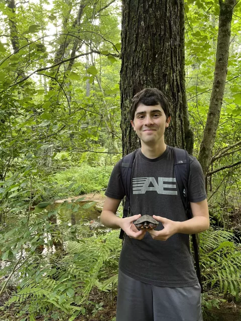 UNH student Jacob McDaniel holding a rescued turtle in the woods before its release