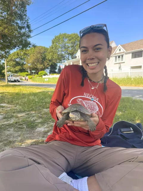 Kalina is sitting on the grass, smiling, holding a turtle