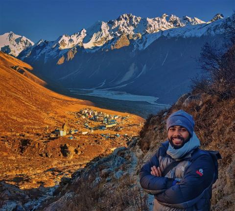 A photo of a man, Sandesh Lamichhane, standing in the mountains in front of a mountain village.