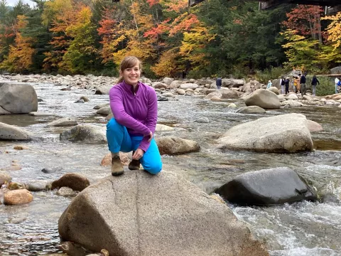 UNH graduate student Kaitlin Van Volkom poses on a rock in a stream in autumn