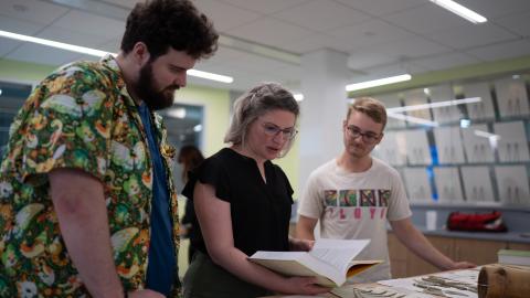 An image of a museum curator looking at plant specimens between two students, both male, standing either side.