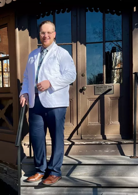 UNH alumni Taylor Gagne poses on steps wearing his white coat from medical school