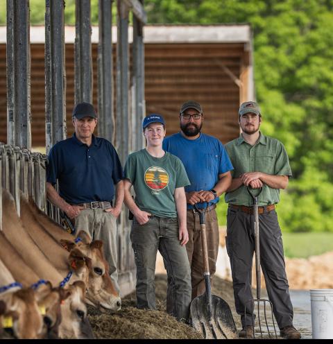The UNH Organic Dairy Research Farm team poses with cows as they eat hay