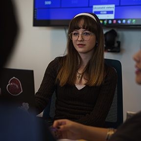 Student with black shirt and white headband listens to another student who is off camera during a peer-led team learning meeting