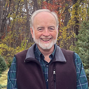 Glenn Coppelman in fleece vest poses among the trees on his Christmas tree farm