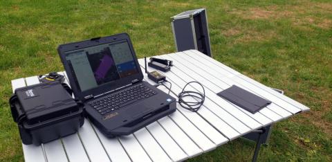 Photo of a table set up a in field. On the table is a laptop with a screen showing a drone flight path.