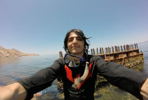 A photo of Marine Biology phd student Miguel de Jesus Gomez Garcia. He's wearing diving gear and behind him is a sunken wreck.